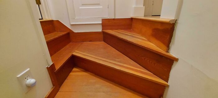 Awful interior design with awkwardly angled wooden stairs in a narrow hallway.