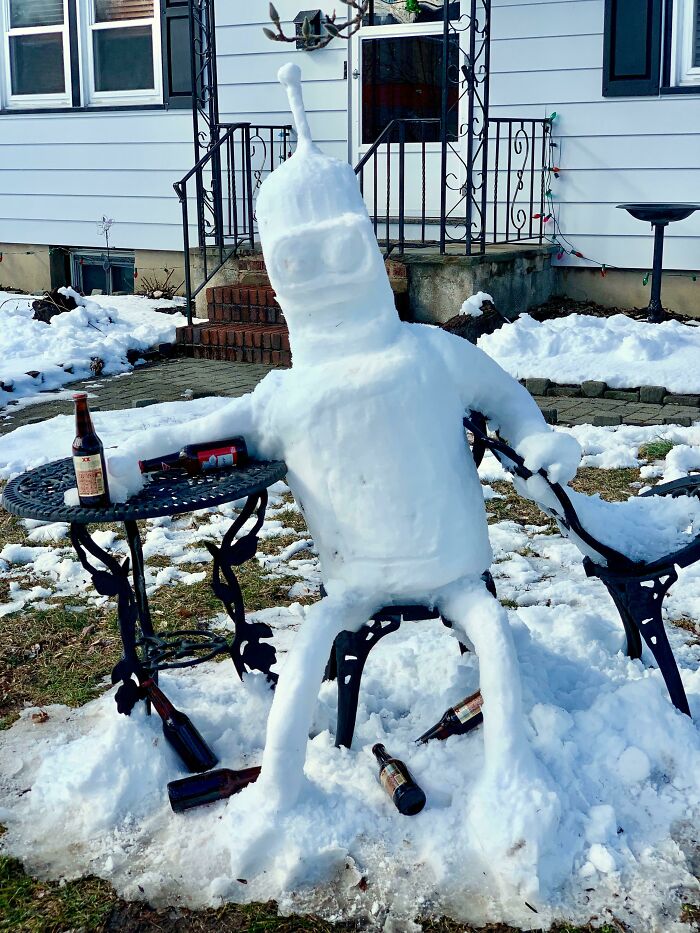 Snowman design shaped like a robot lounging on a chair with beer bottles around in a snowy yard.
