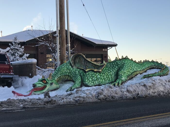 Green dragon snow sculpture with detailed scales and wings, an imaginative snowman design displayed outdoors in winter.