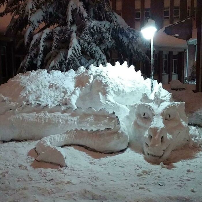Snow dragon snowman design with detailed facial features and scales, created in a snowy outdoor setting under streetlight.
