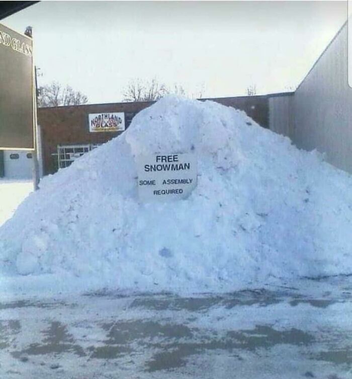 Large pile of snow outside a building with a sign offering a free snowman, some assembly required, snowman designs concept.