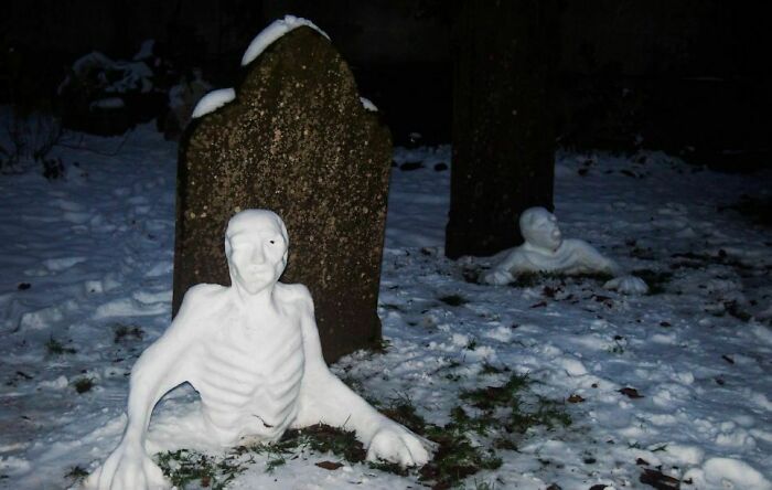 Unique snowman designs shaped like emerging skeletons in a snowy graveyard setting at night.