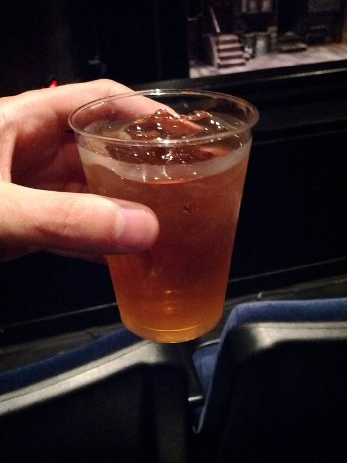 Hand holding a plastic cup with an iced drink, illustrating bartenders in this online group jokingly disclosing drink orders.