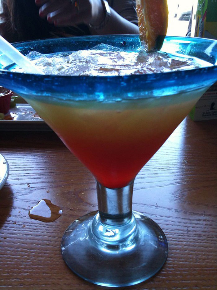 Colorful cocktail in a blue-rimmed glass on a wooden table, representing bartenders sharing drink order insights.