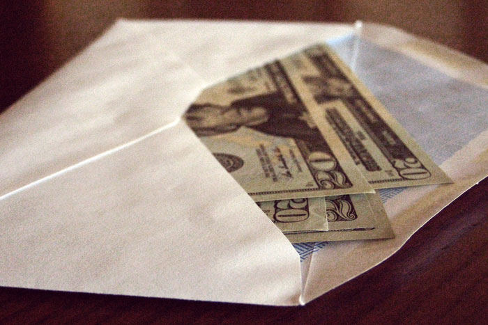 Envelope partially open on wood surface revealing money inside, illustrating aspects of former prisoners' incarceration experience.