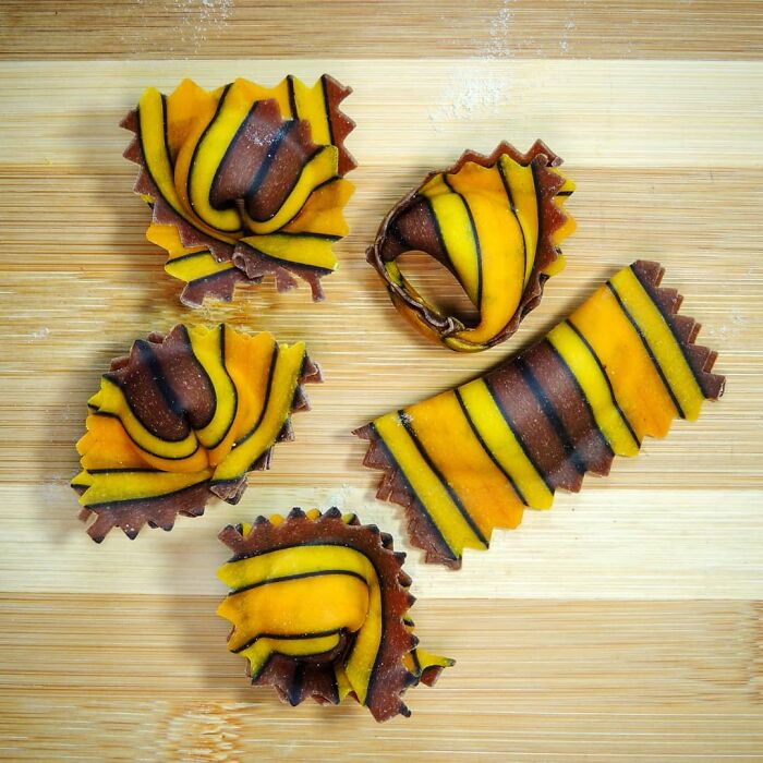 Unique striped pasta designs in yellow, orange, and brown hues arranged on a wooden cutting board.