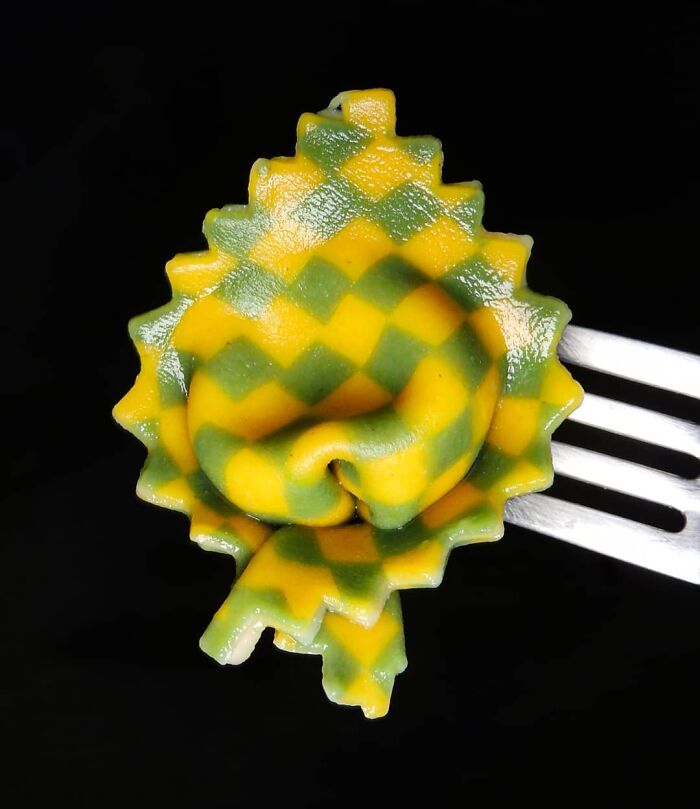 Checkerboard pattern unique pasta design held on a fork, showcasing vibrant green and yellow colors on a black background.
