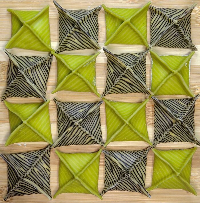 Unique pasta designs in green and black striped patterns arranged neatly on a wooden surface by a creative chef