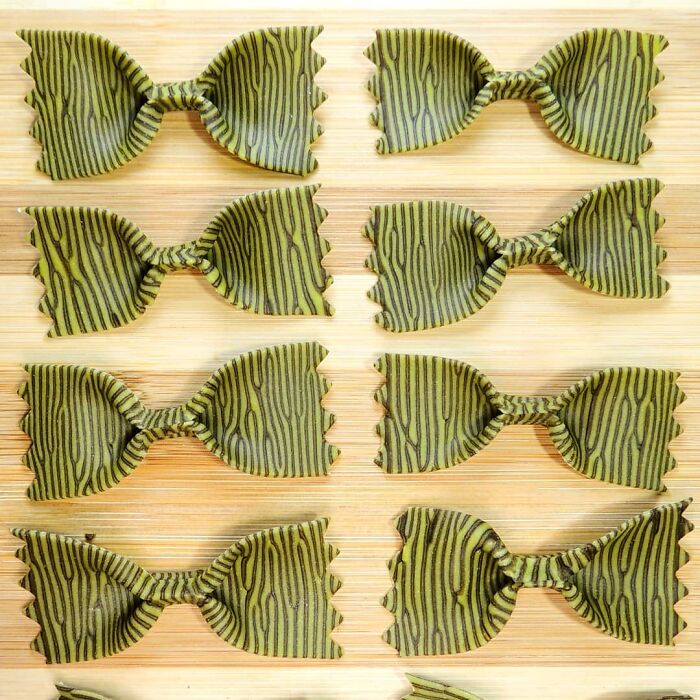 Unique pasta designs shaped like bow ties with black striped patterns on a wooden cutting board, showcasing creative pasta art.