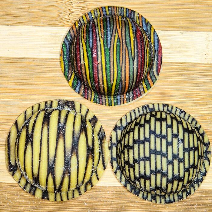 Three unique pasta designs with colorful and black striped patterns on a wooden surface by a creative chef.