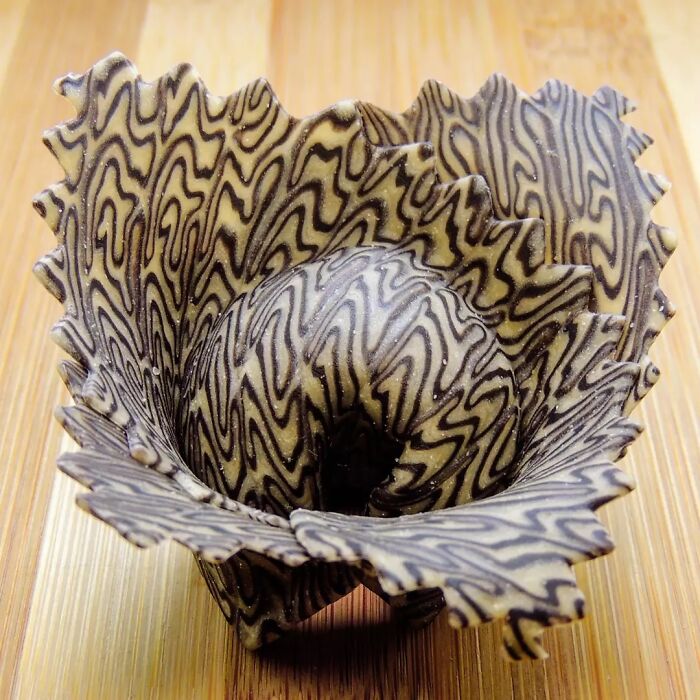 Intricately patterned unique pasta design shaped like a flower with wavy edges on a wooden surface.