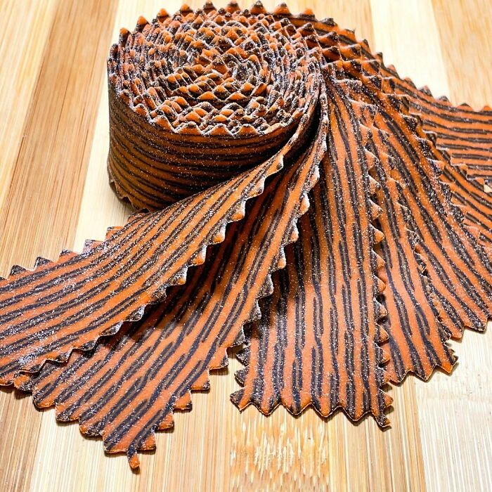 Rolled unique pasta design with black and orange striped pattern by a chef, shown on a wooden surface.