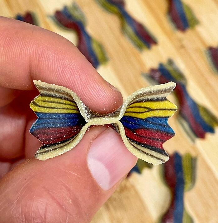 Hand holding a piece of colorful unique pasta design shaped like a bowtie, showcasing vibrant striped patterns.
