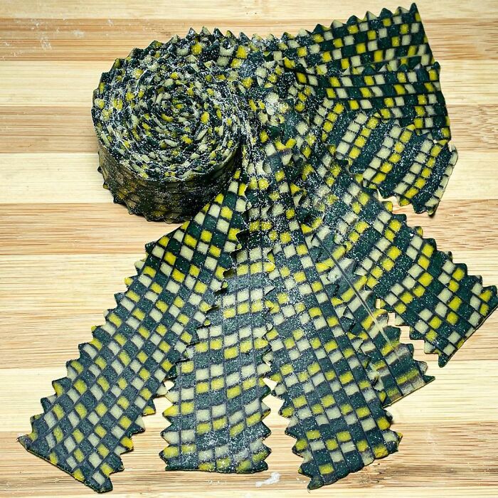 Rolled pasta with a unique checkered pattern featuring dark green and yellow squares on a wooden surface.