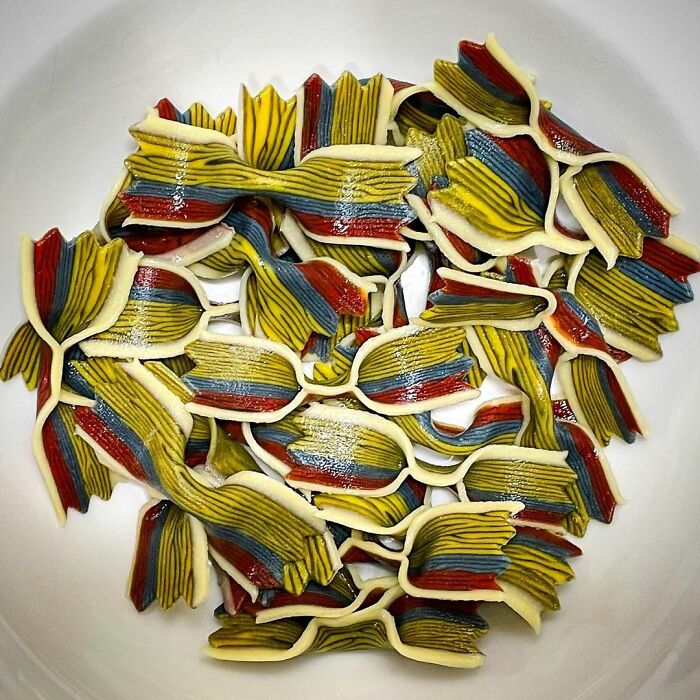 Colorful unique pasta designs shaped like bow ties arranged in a white bowl, showcasing creative pasta art by a chef.