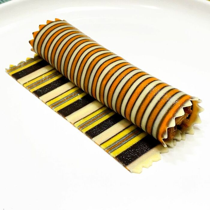Rolled pasta with unique striped design in orange, black, yellow, and white colors showcasing creative pasta designs by chef.
