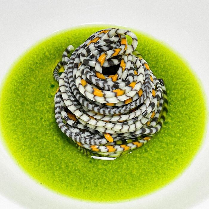 Unique pasta design by a chef with black, white, and orange striped noodles served in a vibrant green sauce.