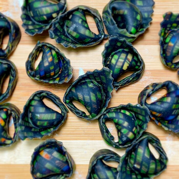 Unique pasta designs with intricate green and black patterns arranged on a wooden surface by a creative chef.