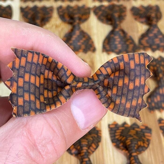 Hand holding unique pasta design shaped like bowtie with orange and black checkered pattern by viral chef.