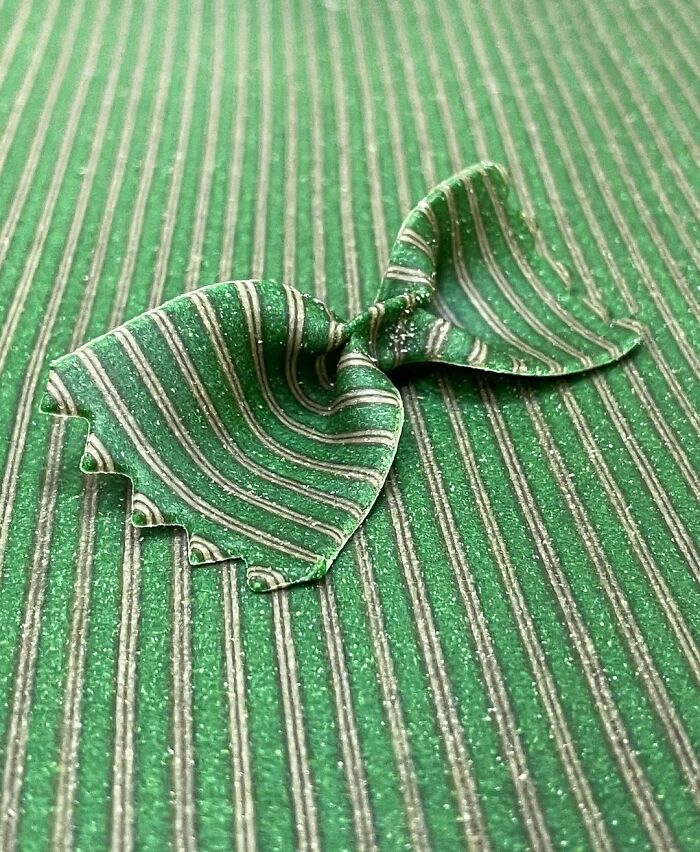 Green striped unique pasta design shaped like butterfly wings on a matching green striped surface by a chef.
