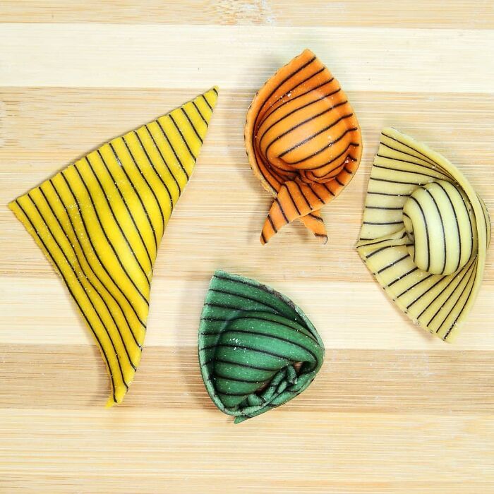 Four unique pasta designs in yellow, orange, green, and beige with black stripes on a wooden surface.