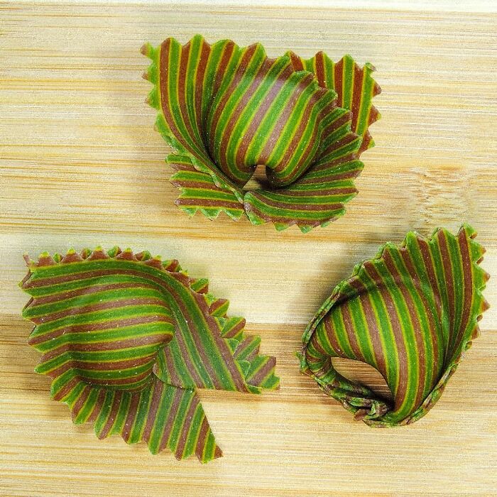 Three unique striped pasta designs with green and red hues placed on a wooden surface by a creative chef.
