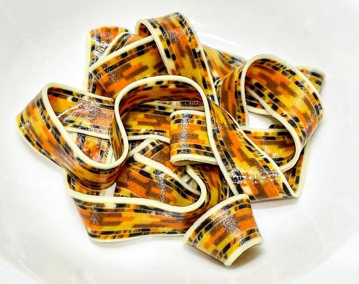 Colorful unique pasta designs with orange, yellow, and black patterns by a chef, displayed on a white plate.