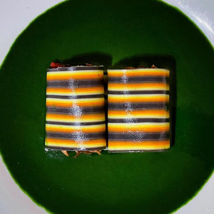 Two striped pasta rolls with vibrant orange, yellow, and black layers served on a plate with green sauce, showcasing unique pasta designs.