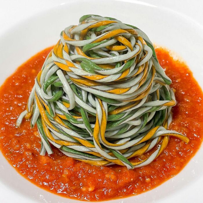 Tri-colored unique pasta design by chef served on a plate with vibrant red tomato sauce in an artistic presentation