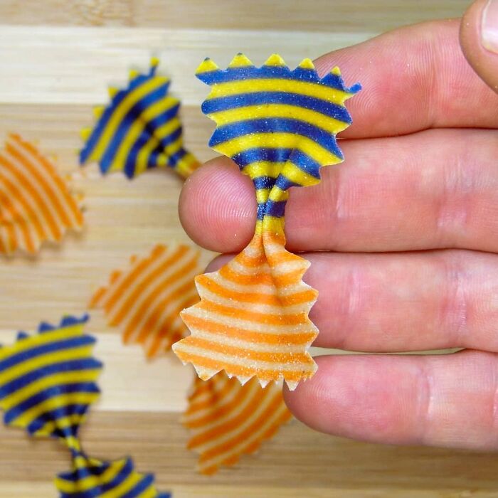 Close-up of a unique striped pasta design held between fingers, showcasing creative pasta designs by a chef.