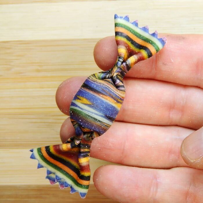 Hand holding a colorful striped pasta shaped like wrapped candy, showcasing unique pasta designs by a chef.