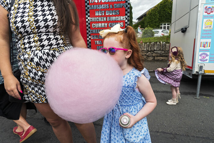 Young girl with large pink cotton candy and sunglasses at a street food stall in a powerful street photo.