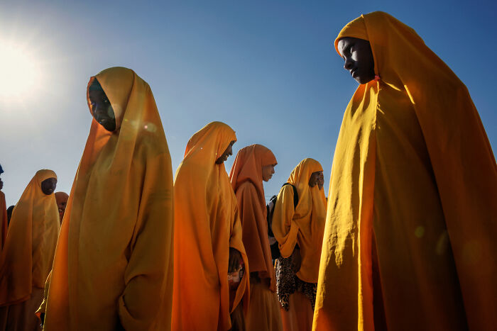 Group of women in yellow robes walking outdoors under bright sunlight, captured in powerful street photos style.