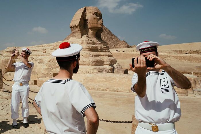 Three sailors in white uniforms taking photos near the Great Sphinx in a powerful street photo setting.