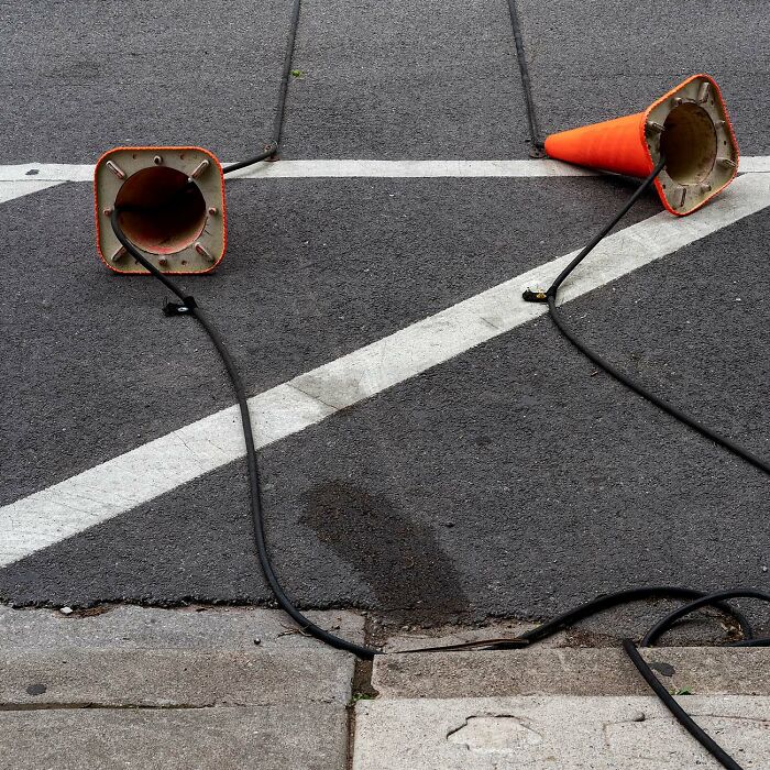 Two fallen street cones tangled with black cables on an asphalt road with white painted lines, urban street scene.