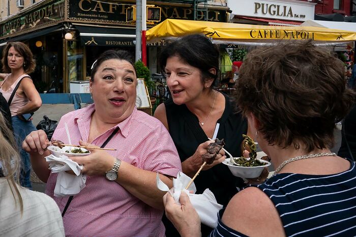 Group of women enjoying street food outdoors in front of a cafe, captured in a powerful street photo moment.