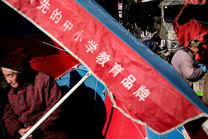 Elderly people sitting beside umbrellas on a busy street in a candid street photo capturing daily urban life moments.
