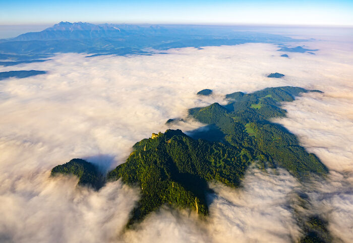 Aerial view of Poland’s diverse landscape with green mountains rising above a sea of clouds on a bright day.