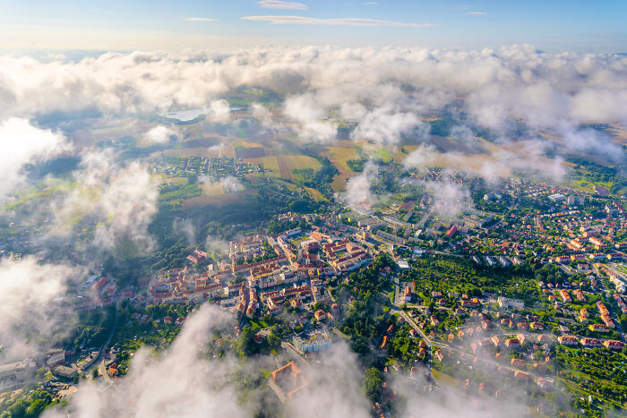 Aerial view of a modern and diverse city in Poland with green areas and clouds partially covering the landscape.