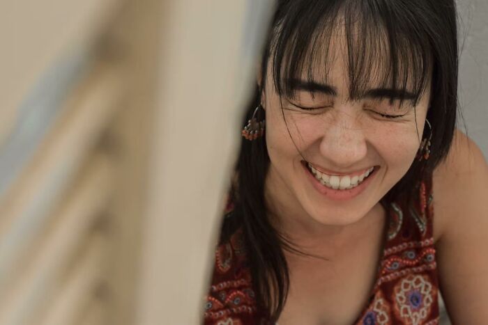 Young woman laughing with eyes closed, wearing a patterned sleeveless top, capturing a moment of lighthearted encounter.