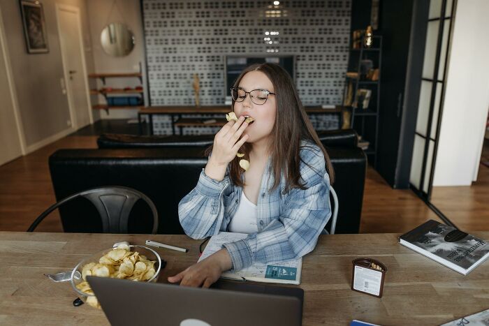 Young woman eating chips while using laptop, illustrating people encounters that made others think about intelligence levels.