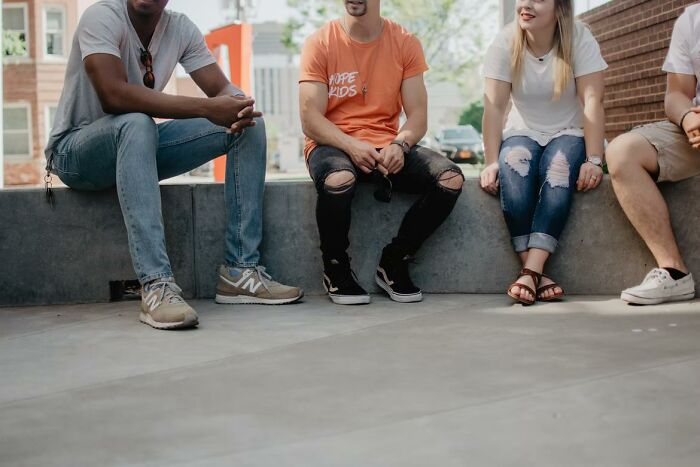Four young adults sitting outdoors on a concrete ledge, sharing casual moments in a relaxed urban setting.