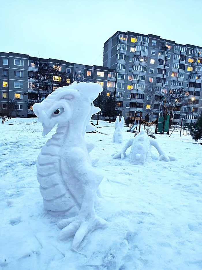 Snowman designs shaped like a dragon and creatures displayed on snow in a residential area with apartment buildings.