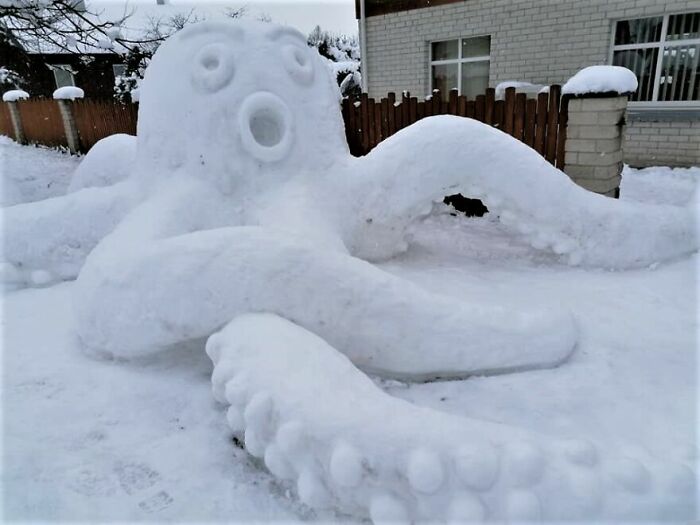 Snowman design shaped like a large octopus with detailed tentacles made from snow in a snowy yard.