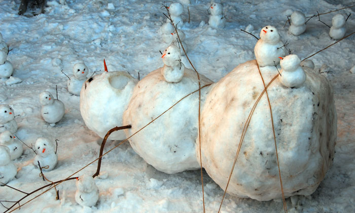 Various creative snowman designs made from compact snowballs with stick arms and carrot noses in a snowy outdoor setting