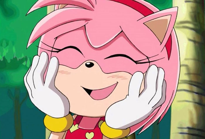 Cute animated character with pink hair, cat ears, and gloves, smiling joyfully in a forest background.