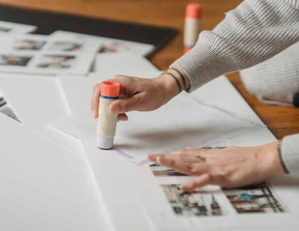 Person using glue stick to assemble a photo album, focusing on creativity and craft.