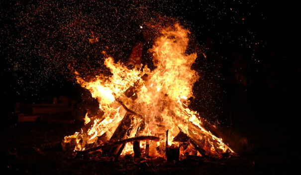 "Large bonfire at night, flames crackling amid sparks with a dark background, capturing a dramatic fiery scene."