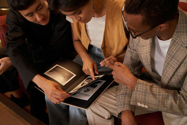 Three friends sharing a photo album, pointing and discussing dark humor.