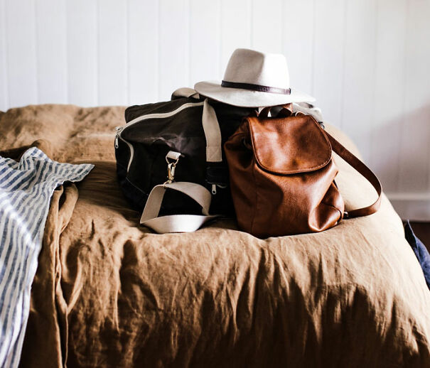 Brown leather backpack and hat on bed next to a striped cloth, suggesting travel or adventure.